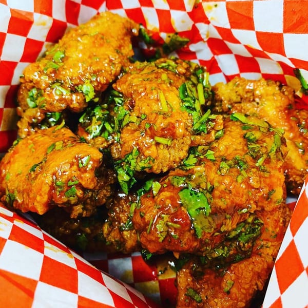 Vons Chicken Waimalu's fried chicken wings, glazed and topped with fresh green herbs, in a red and white checkered basket.