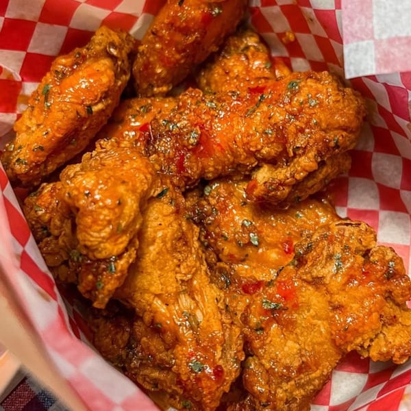 Close-up of Vons Chicken Waimalu's fried chicken pieces, coated in a glossy orange sauce with herbs.