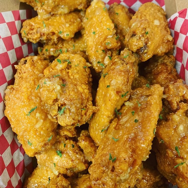 Close-up of Vons Chicken's golden fried chicken wings with sauce and parsley in a red checkered basket.