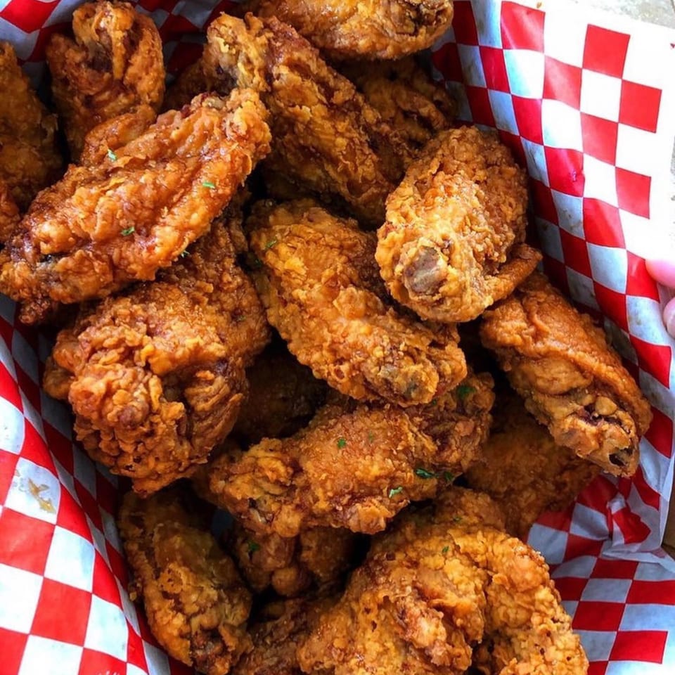 Crispy golden-brown fried chicken pieces, some with visible herbs, in a red and white checkered paper-lined basket.