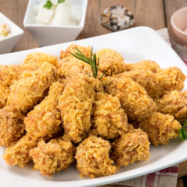 A white platter piled high with golden-brown fried chicken pieces, garnished with a sprig of rosemary.