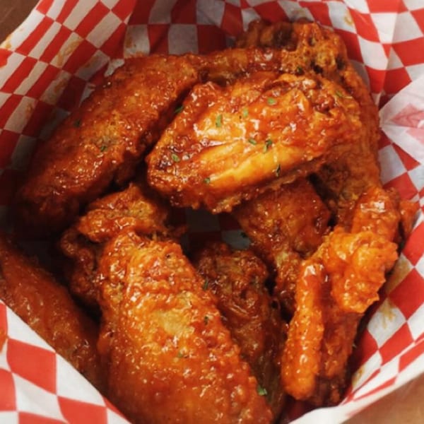 Close-up of Vons Chicken Waimalu's fried chicken wings, coated in a glossy orange sauce, in a red and white checkered basket.
