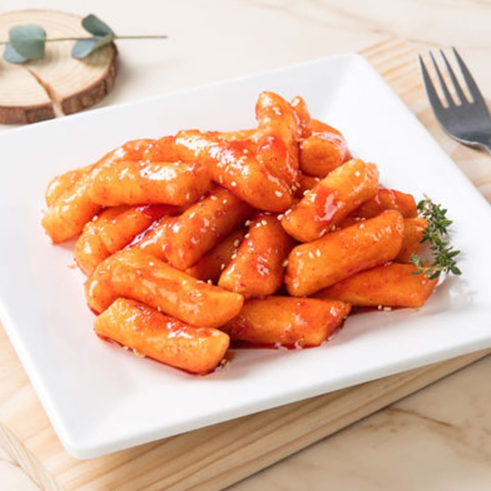 Plate of Vons Chicken Waimalu's spicy tteokbokki, garnished with sesame seeds and a sprig of thyme.