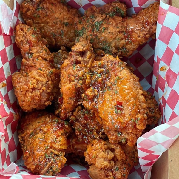 Close-up of Vons Chicken's fried chicken pieces, glistening with sauce and sprinkled with herbs in a red and white checkered box.